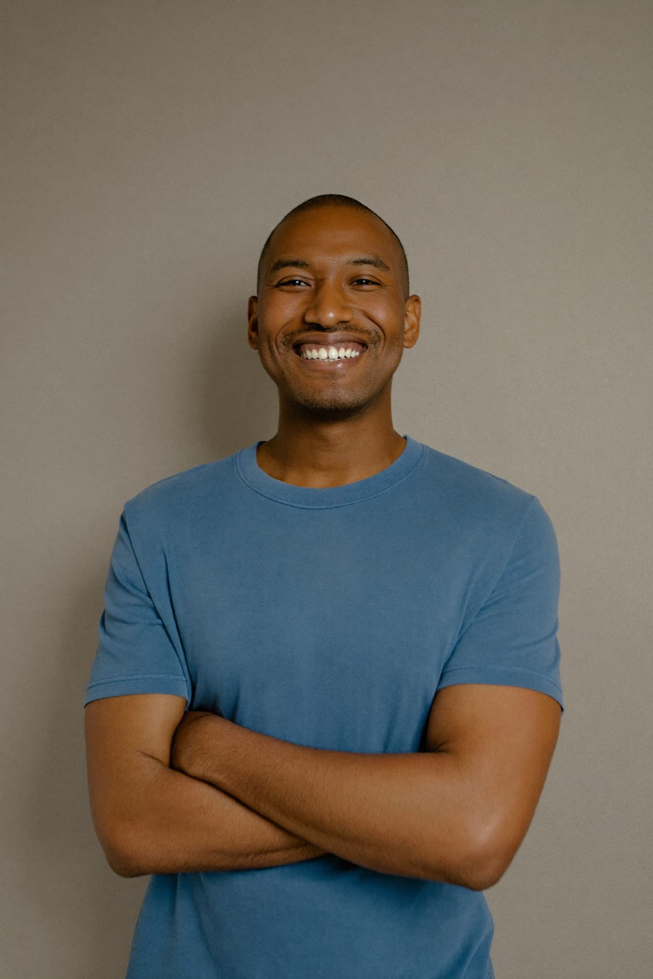 A man in a blue t-shirt smiling with his arms crossed