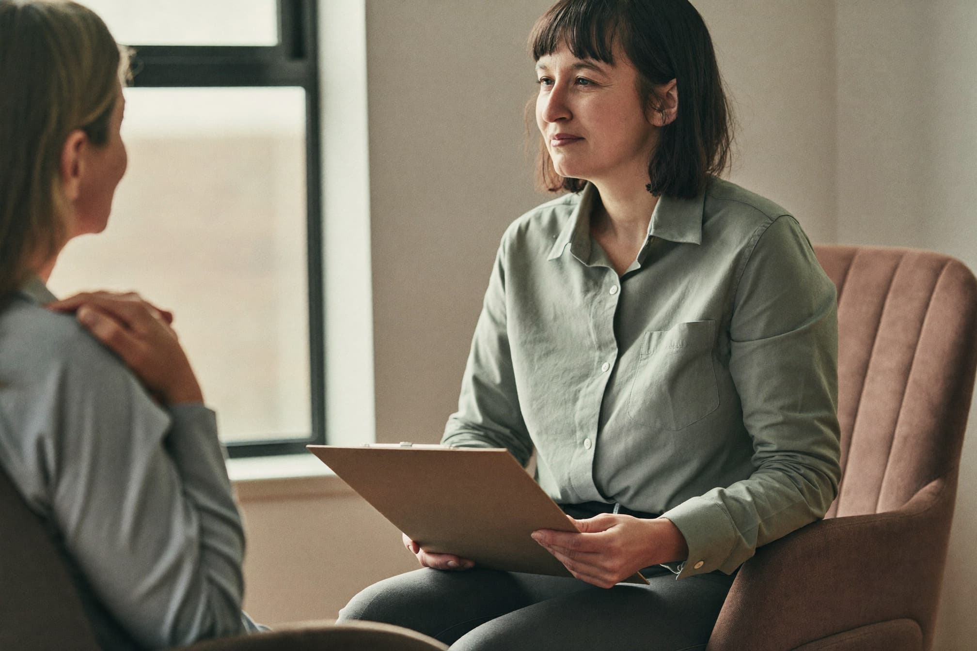 A counselor with a clipboard listens to a seated patient