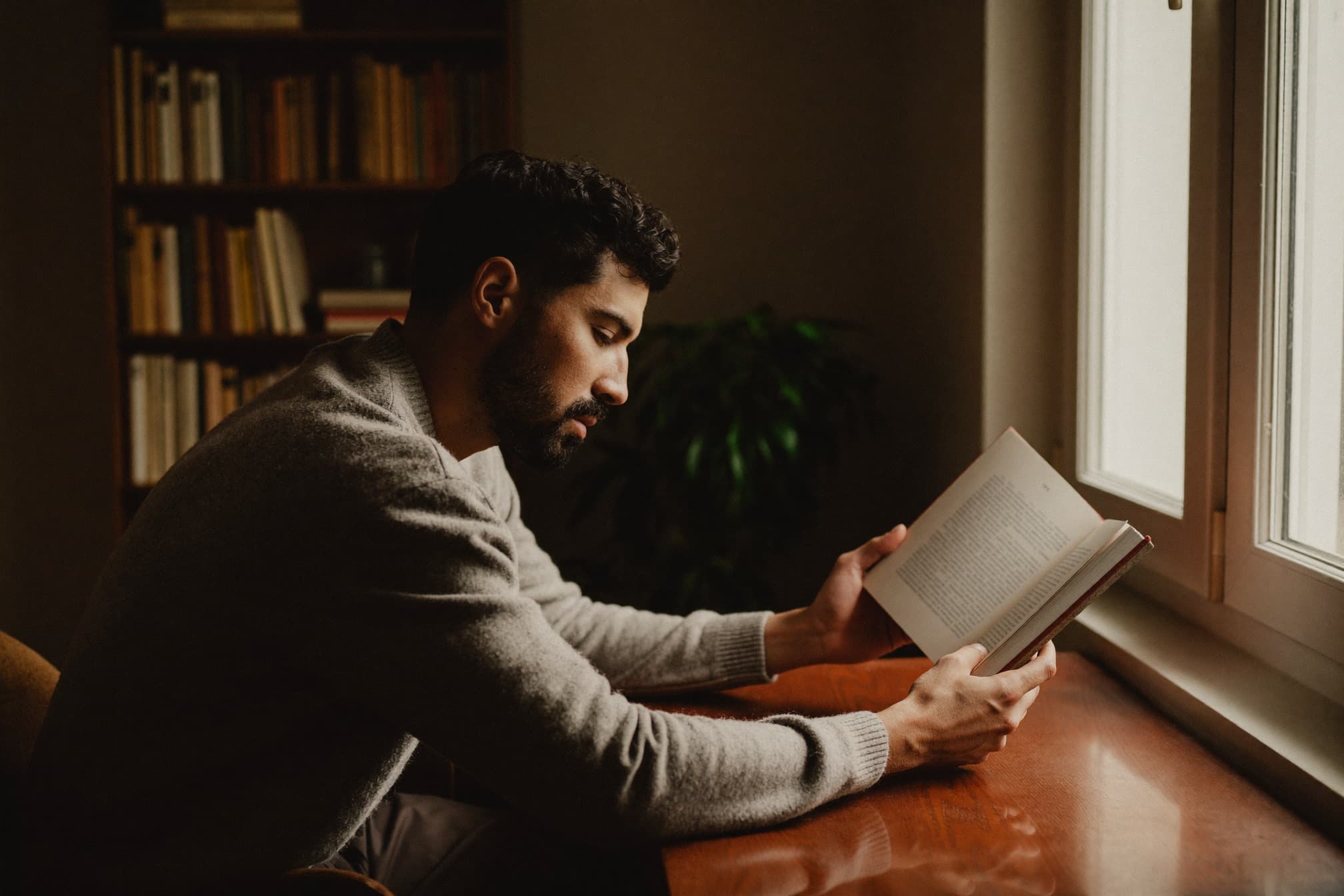 A man reads quietly at a warm wooden desk